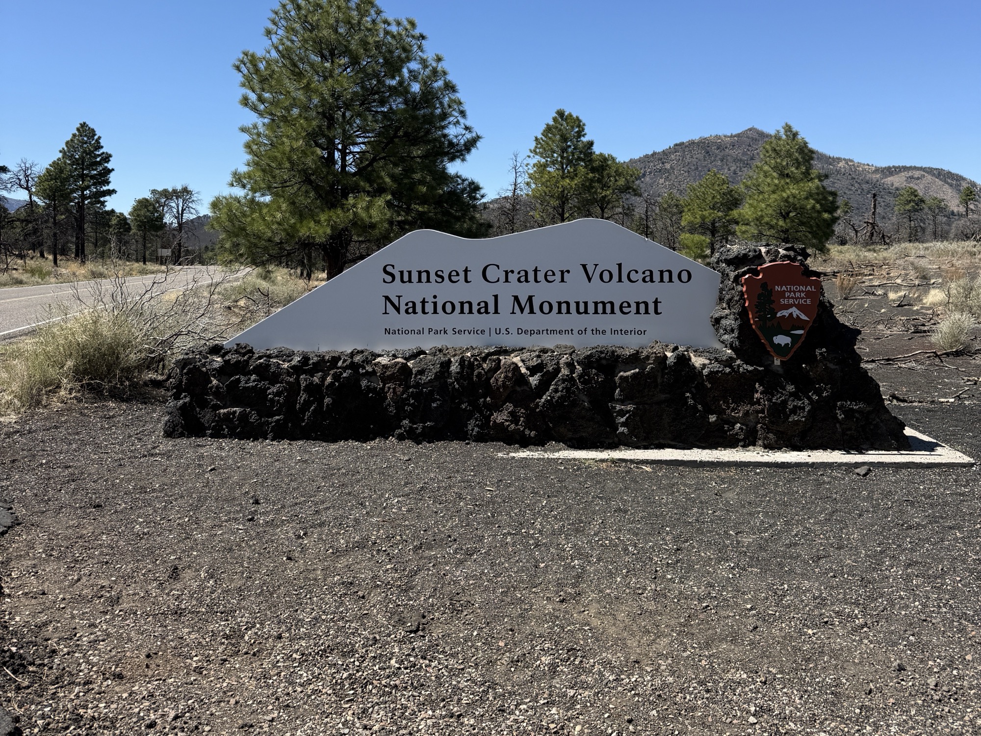 The Sunset Crater Volcano National Monument entrance sign beside the paved scenic road in Northern Arizona.