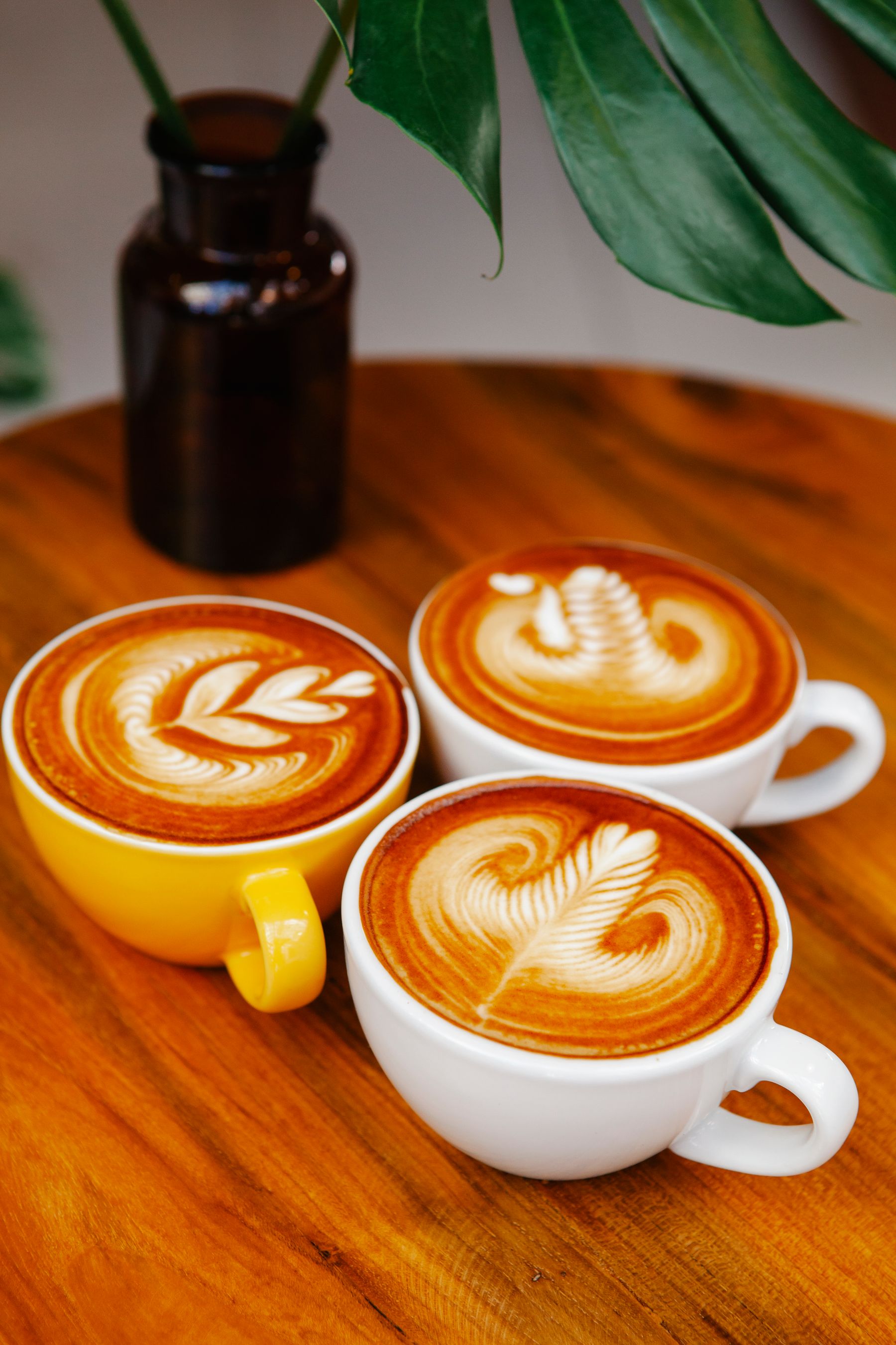 Colorful cups of latte art on a wooden café table.