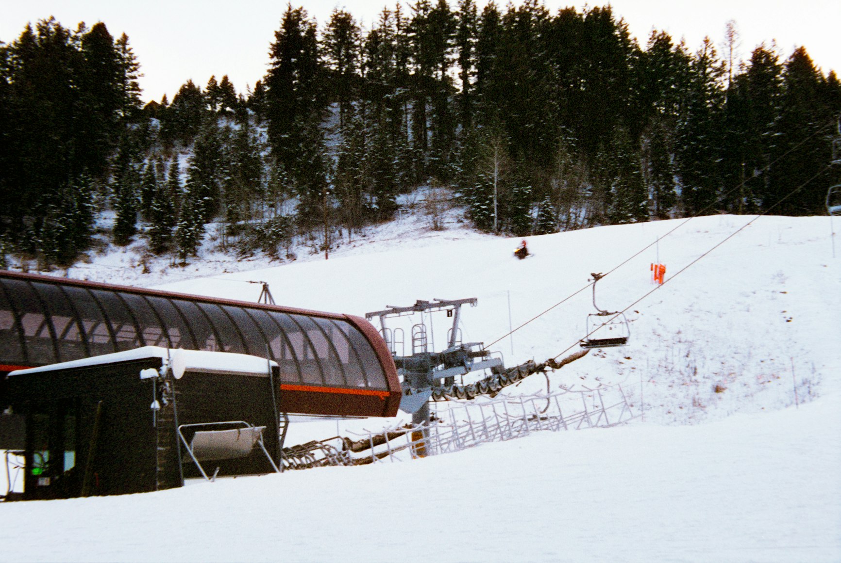 Chairlift station and snowy ski slope surrounded by pine trees.