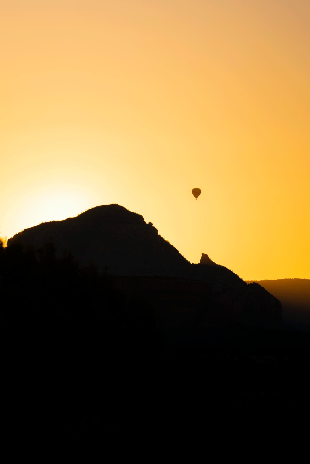 A hot-air balloon floating above the Sedona red rocks at sunrise