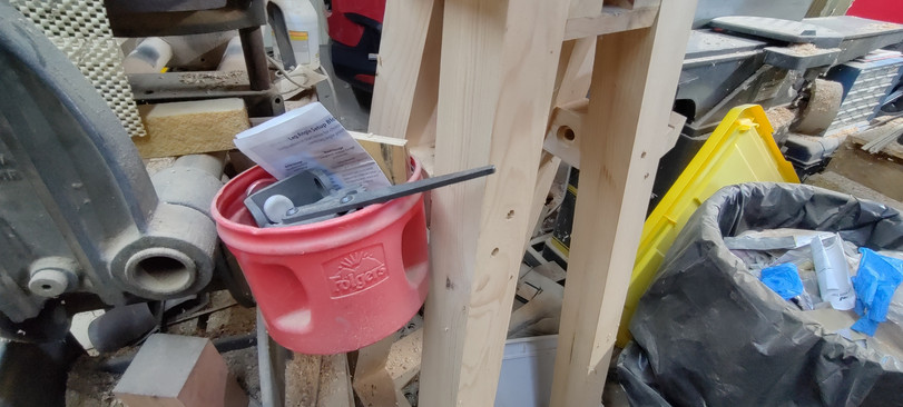 Showing a plastic coffee bucket screwed to the side of the stand with misc pieces in it