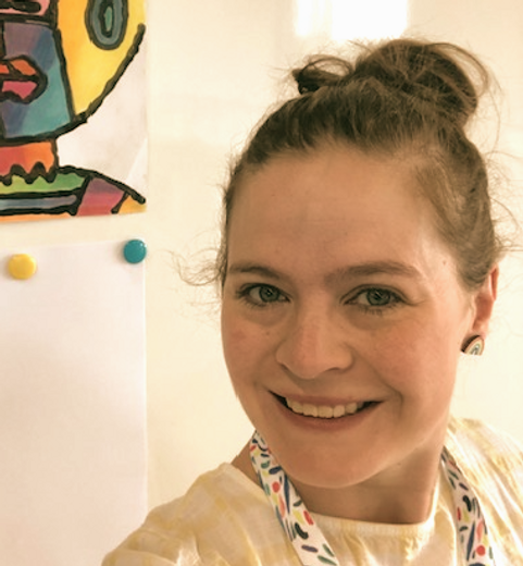 Smiling teacher next to colourful student artwork.