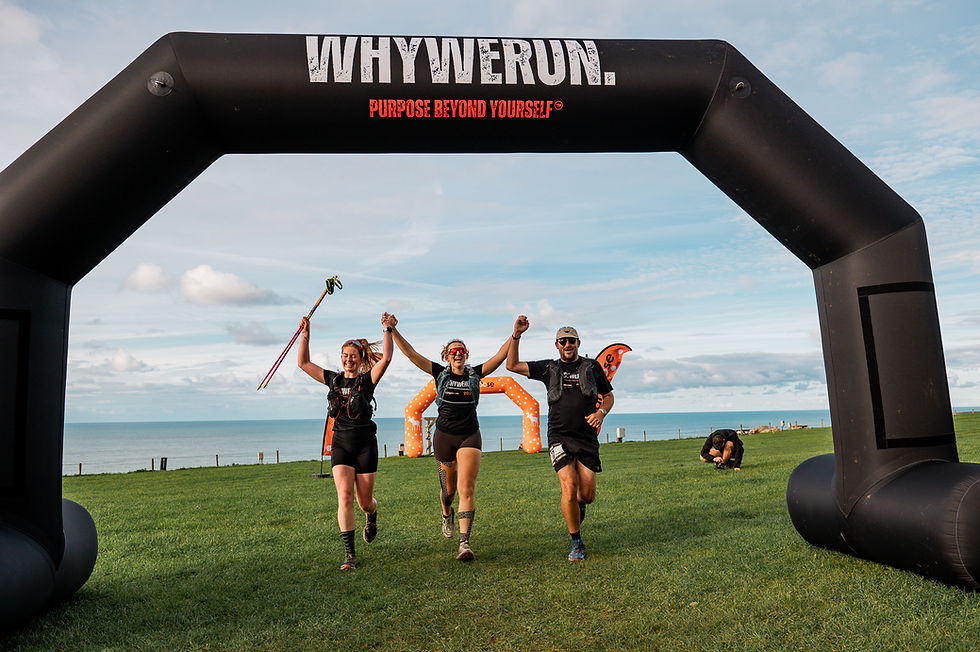 Two women and one man crossing the finish line of the WhyWeRun ultramarathon with their arms in the air