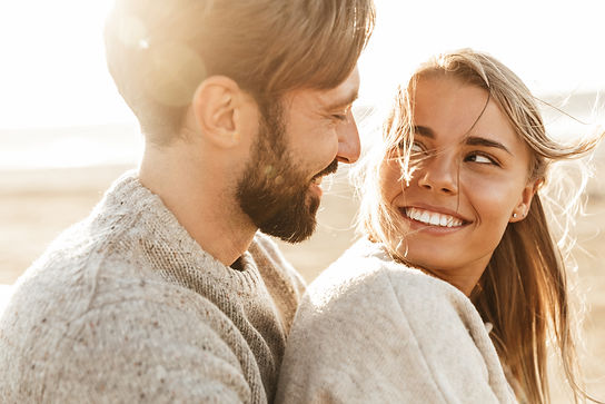 Close up of a smiling beautiful young couple embracing while standing at the beach.jpg