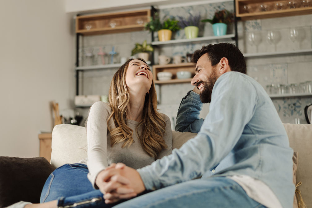 Couple sitting on the couch holding hands and laughing togehter