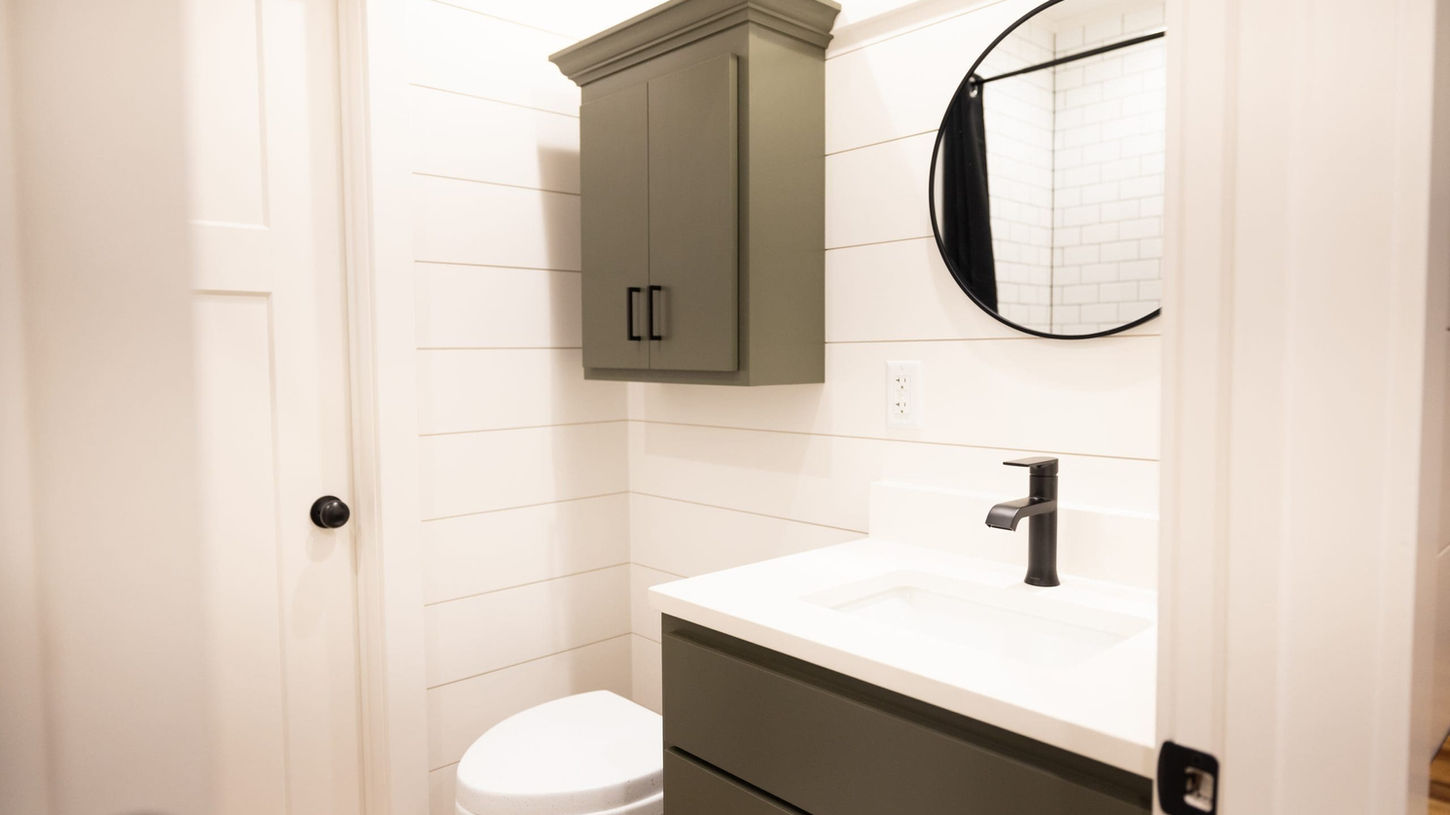 Clean modern bathroom with olive green vanity, white shiplap walls, round mirror.
