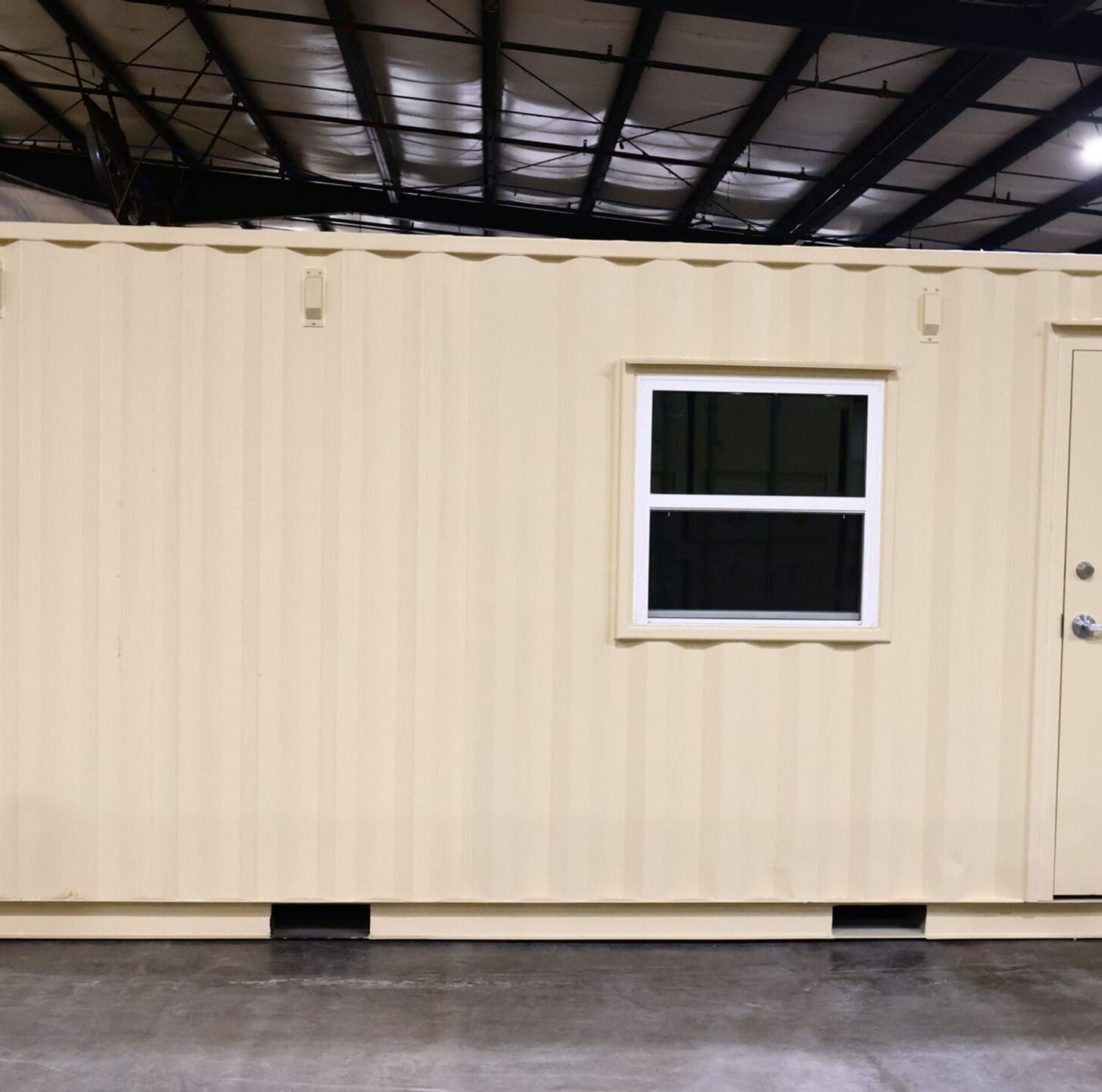 Beige shipping container modified with a window and door, indoors.