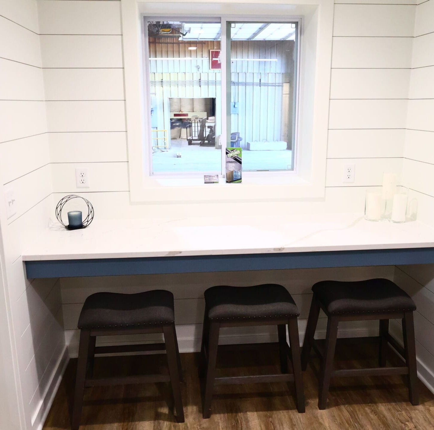 Basement kitchen bar area with egress window, white counter, three stools.