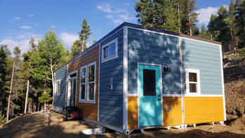Modern tiny house, blue and wood siding, teal door, mountain setting.