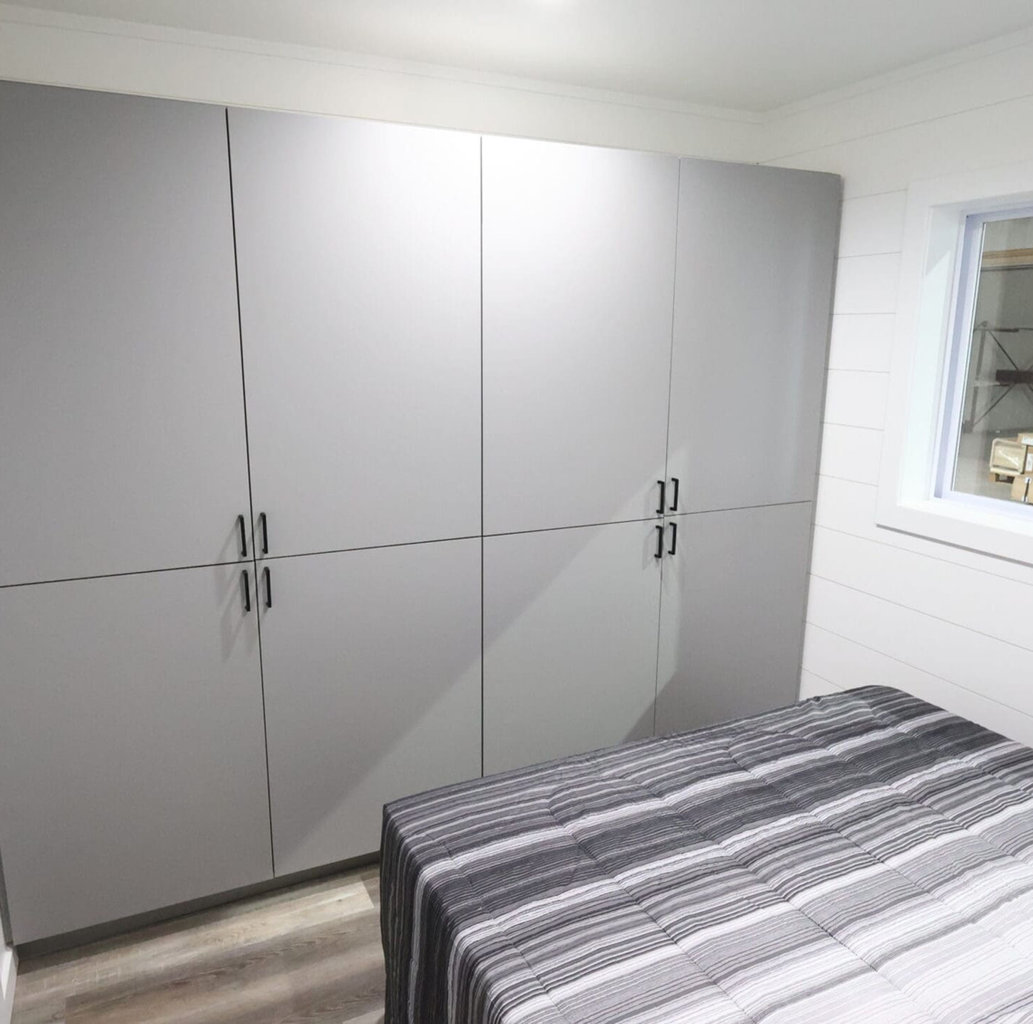 Modern bedroom features sleek gray cabinets, striped bed, and small window.