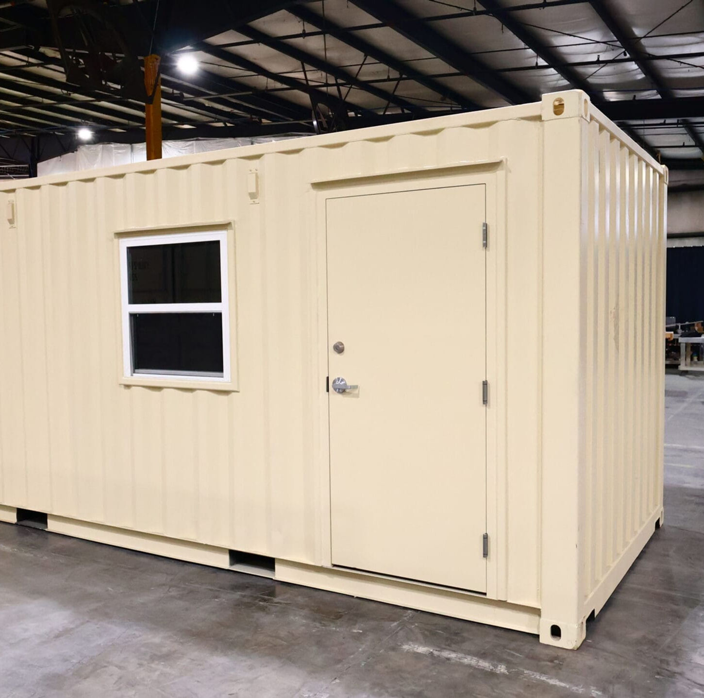 Beige shipping container office unit inside a large industrial warehouse.
