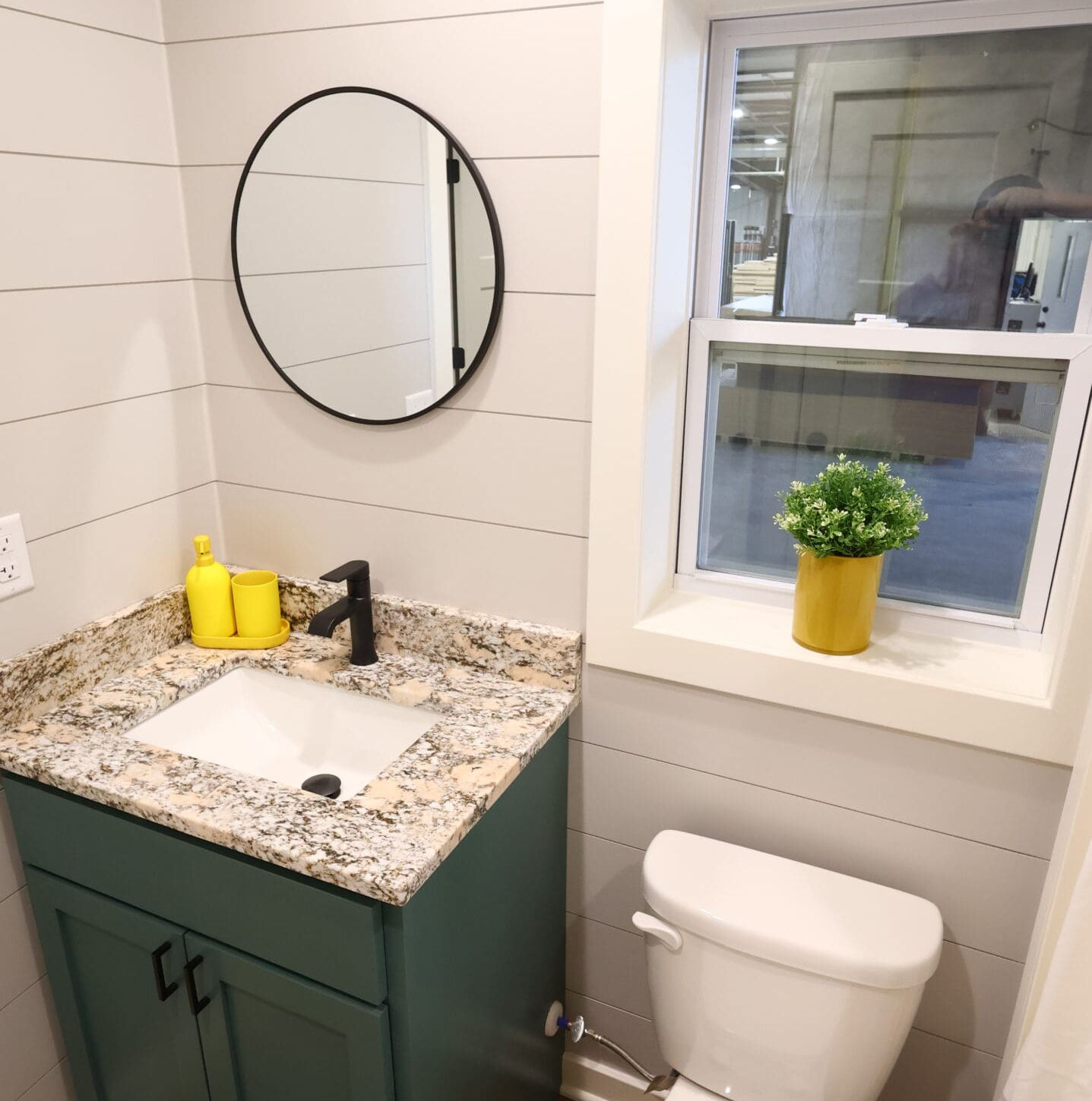 Renovated bathroom features shiplap walls, teal vanity, granite counter, round mirror.