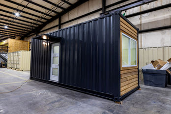 Modified shipping container unit, black metal, wood siding, inside warehouse.