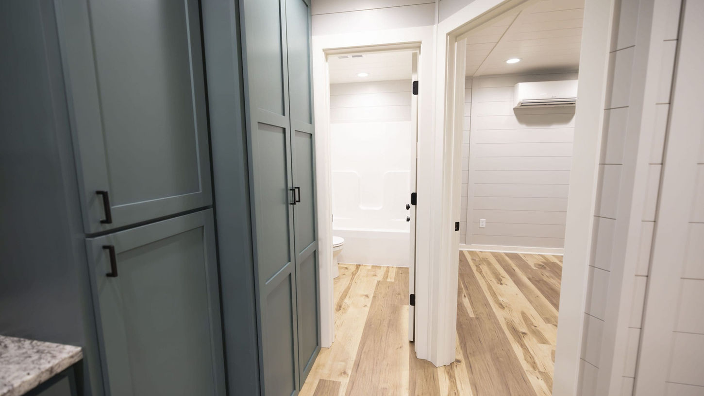 Hallway with light wood flooring, blue-grey cabinets, and view to bathroom.