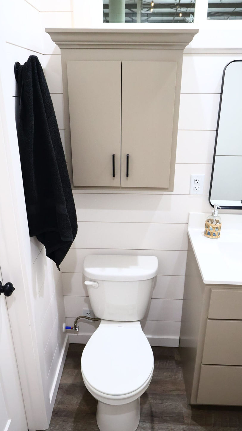 White toilet, beige cabinet, shiplap walls in a small bathroom