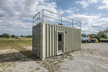 Light green modified shipping container building with rooftop access platform.