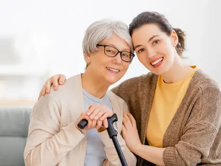 Smiling caregiver embracing happy senior woman with a walking cane indoors.