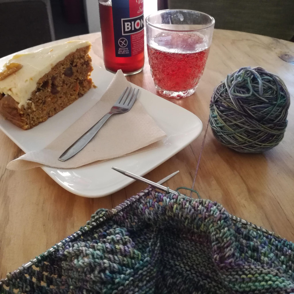 Knitting Yarn and Needles on a Cafe Table with cake and a pink drink