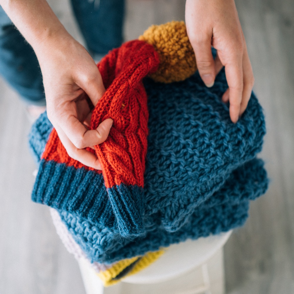 A stack of blue, red and yellow knitwear with a white woman's hand lightly touching them