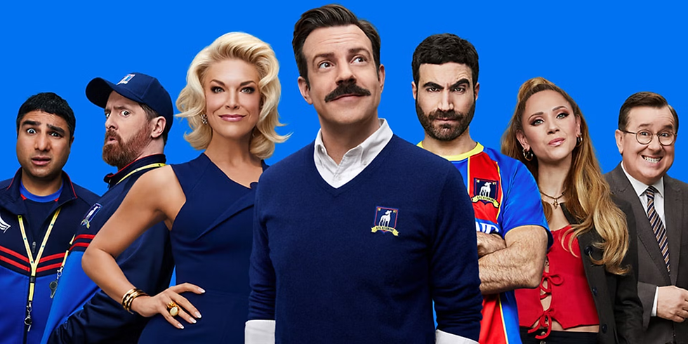 Seven smiling and serious people (Ted, Rebecca, Roy, Beard, Keeley, Nathan, and Higgins) stand against a blue background, wearing colorful outfits. The mood is upbeat and lighthearted.