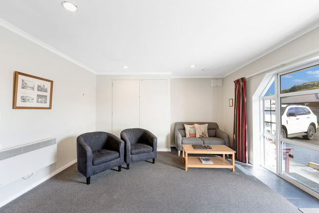 Motel room with two single chairs and lounge with queen bed hidden in cupboard behind chairs.