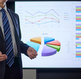 Presenter in a suit pointing to a screen showing line and pie charts