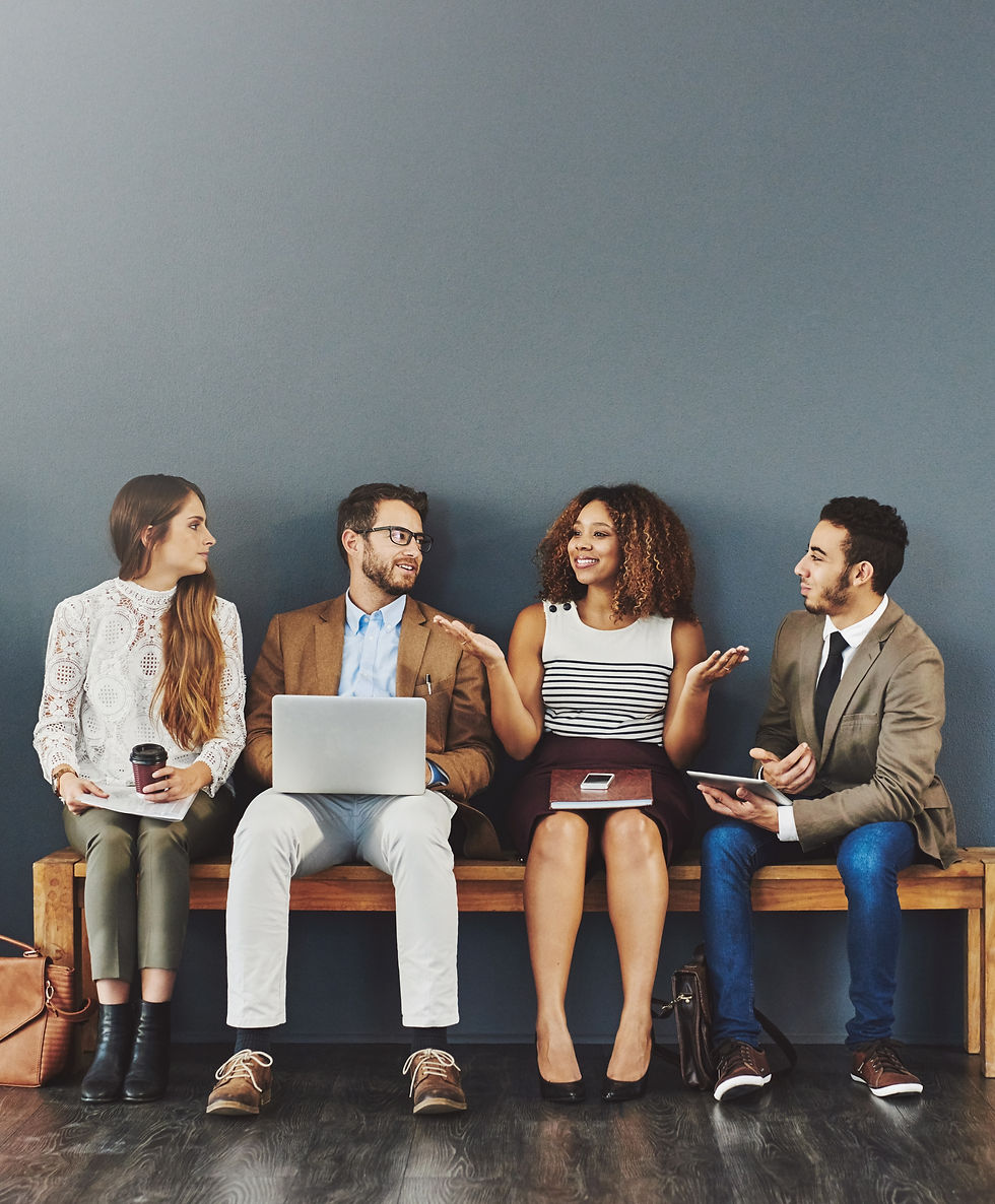 Four young individuals sitting on a bench with notebooks, ipads, laptop and coffee in hand having an engaged conversation.