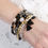 Miniatura: Woman's wrist featuring several stacked beaded bracelets; black, gold, and white AndyClyde's