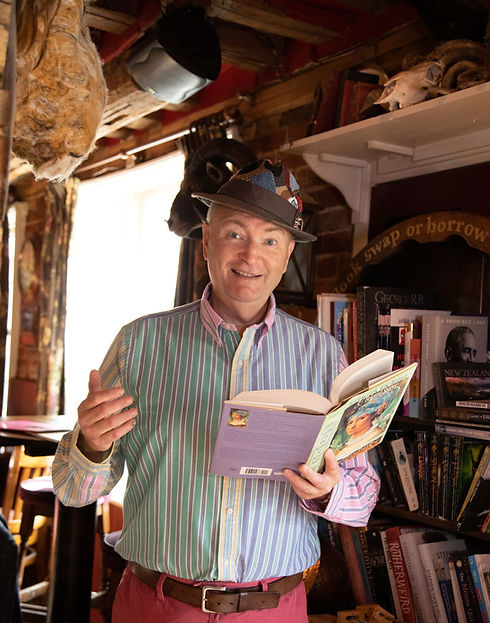 Andy wearing a bright stripy shirt and a colourful hat, reading a book outloud