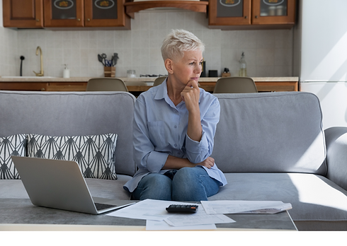 Older lady sat on a sofa, looking pensive, she is facing away from the camera, wearing denim jeans and a pale blue shirt