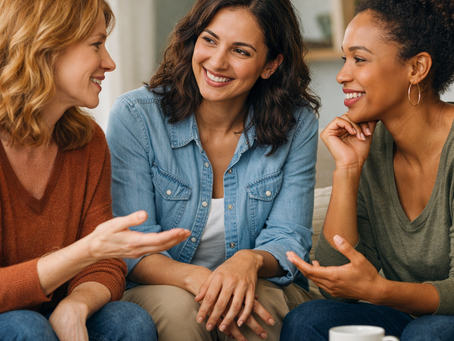 Tres mujeres sentadas juntas en un sofá, sonriendo y conversando mientras toman café, representando una conversación de apoyo sobre decisiones de vida y la maternidad.