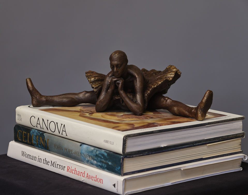 Interior sculpture of a ballerina in a stretching seated position with chin resting on her hands