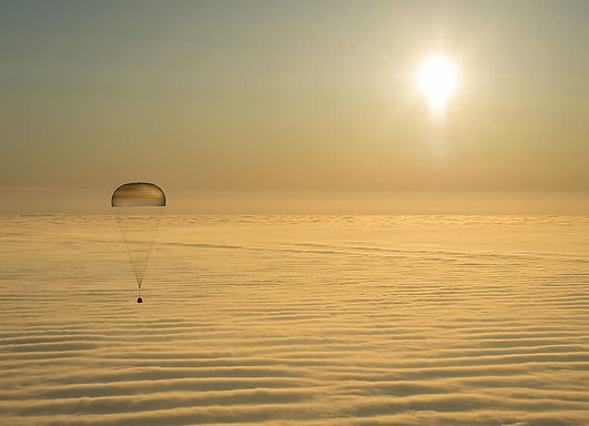 Space capsule on a parachute drifts over the ocean at sunset.