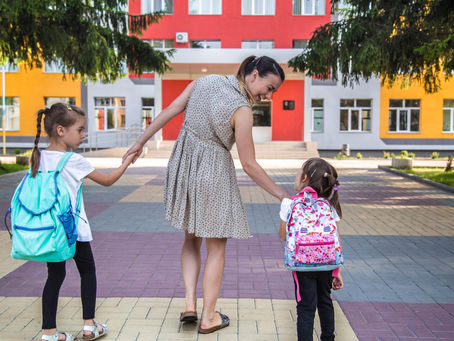 Mother walking two young children with backpacks toward a colorful school, representing readiness for Pre-K in Pembroke Pines, Florida.