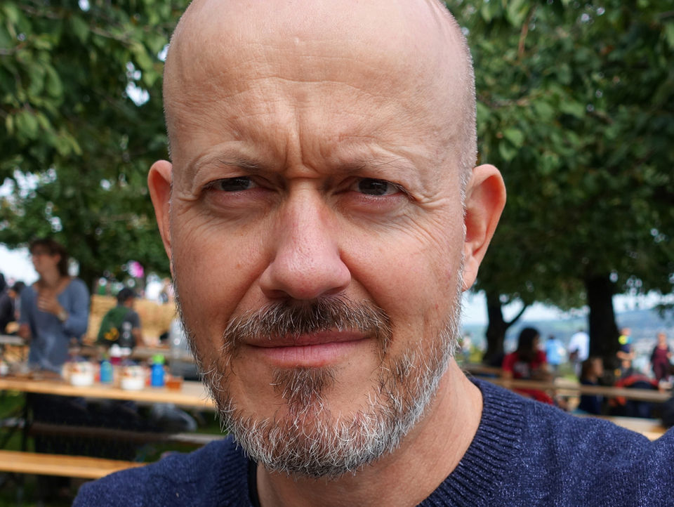 Nahaufnahme portrait Philippe Nauer, Mann mit Bart lächelt vor Bäumen im Freien.