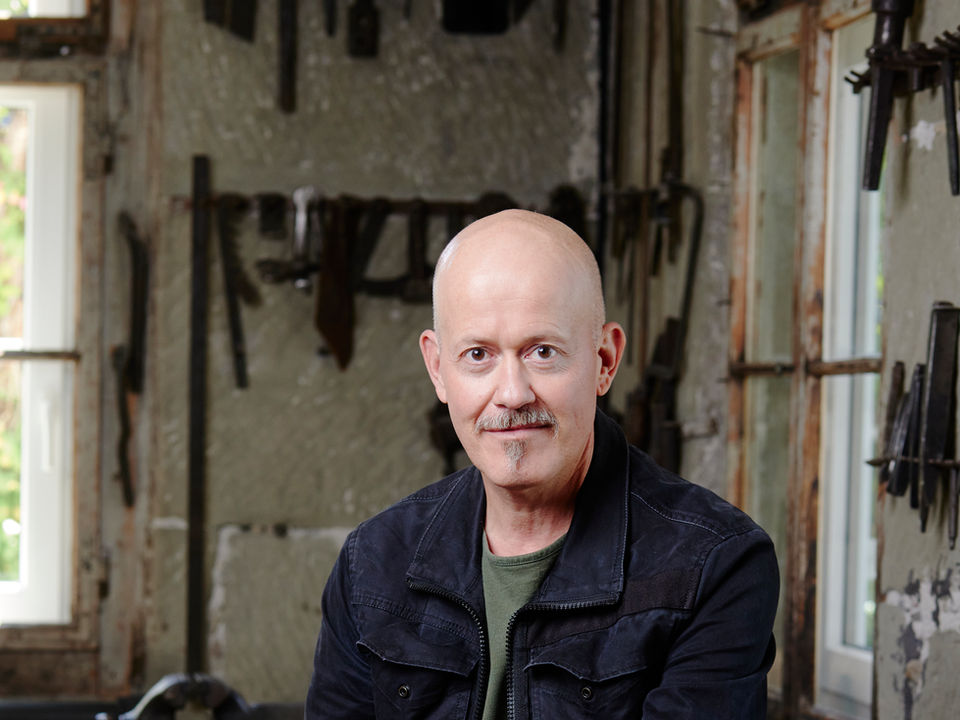 Portrait of Philippe Nauer, smiling, in a workshop, background with tools.