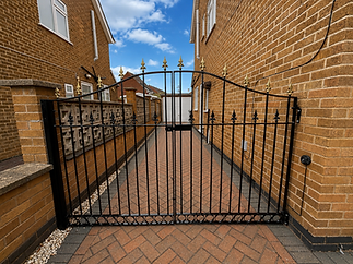 Black ornamental iron gates with gold finials between brick residential buildings