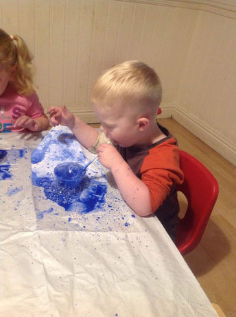 child at a table blowing blue paint bubbles
