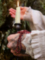 Red garnet beaded necklace draped over a hand holding a candle