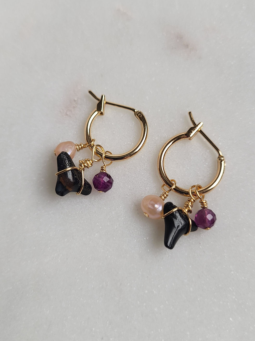 Thumbnail: Gold hoop earrings with wire wrapped amethyst beads, pink freshwater pearls, and fossilized shark teeth
