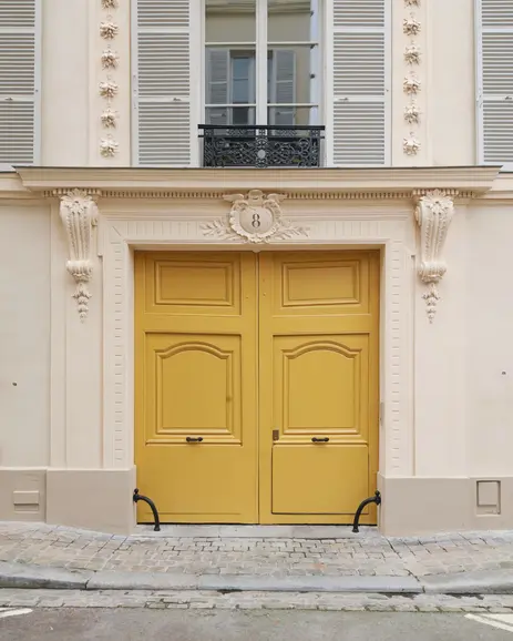 Architecte ravalement Versailles : porte cochère jaune restaurée Maison du Modèle 8 rue Tournelles, menuiserie bois double vantaux XVIIIe siècle, encadrement modénature consoles florales, persiennes gris, pavés anciens - Cabinet Antoine de Gironde architecte Versailles restauration façade secteur protégé label Fondation Patrimoine