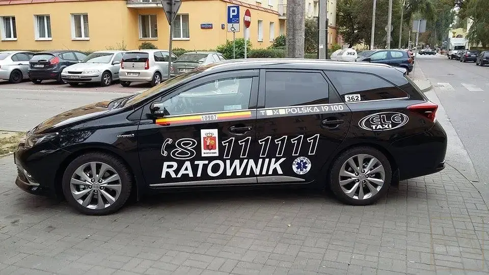 A black car with the words "Rescuer" and a phone number on it is visible. The background is a street lined with parked cars and low-rise buildings.