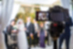 Camera focuses on a wedding party with a blurred backdrop of fairy lights. The screen shows people posing, capturing a joyful moment.