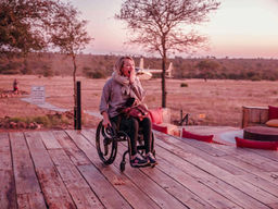 Sophie Morgan looking amazed sitting in her wheelchair on a deck at Ximuwu game lodge. There is a helicopter in the background