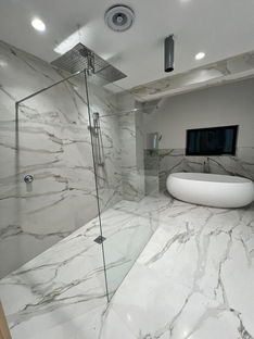 Luxurious modern bathroom featuring marble tiles, a freestanding tub, and glass shower.