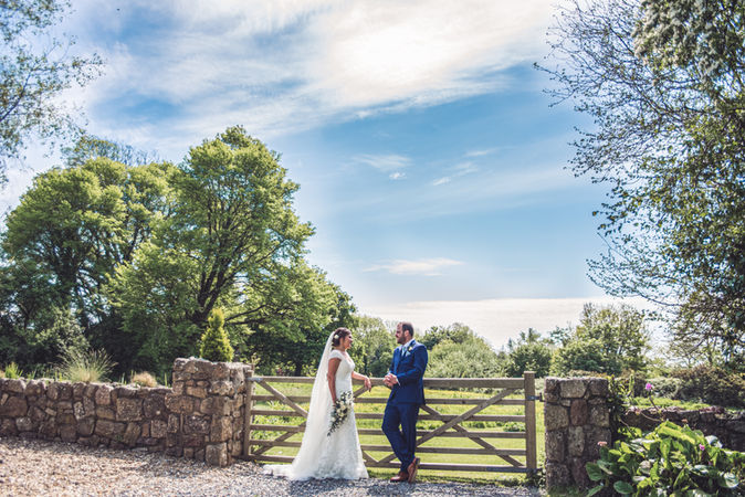 The bride and groom stand by the gates in the grounds of the king Arthur at a wedding at the King Arthur Hotel, Gower, Swansea, photographed by Swansea Wedding Photographer, Katy Tainton Photography