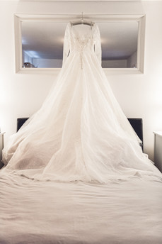 A long sleeved wedding dress hangs over a bed at a wedding at the Oxwich Bay Hotel, Gower, photographed by Swansea wedding photographer, Katy Tainton Photography