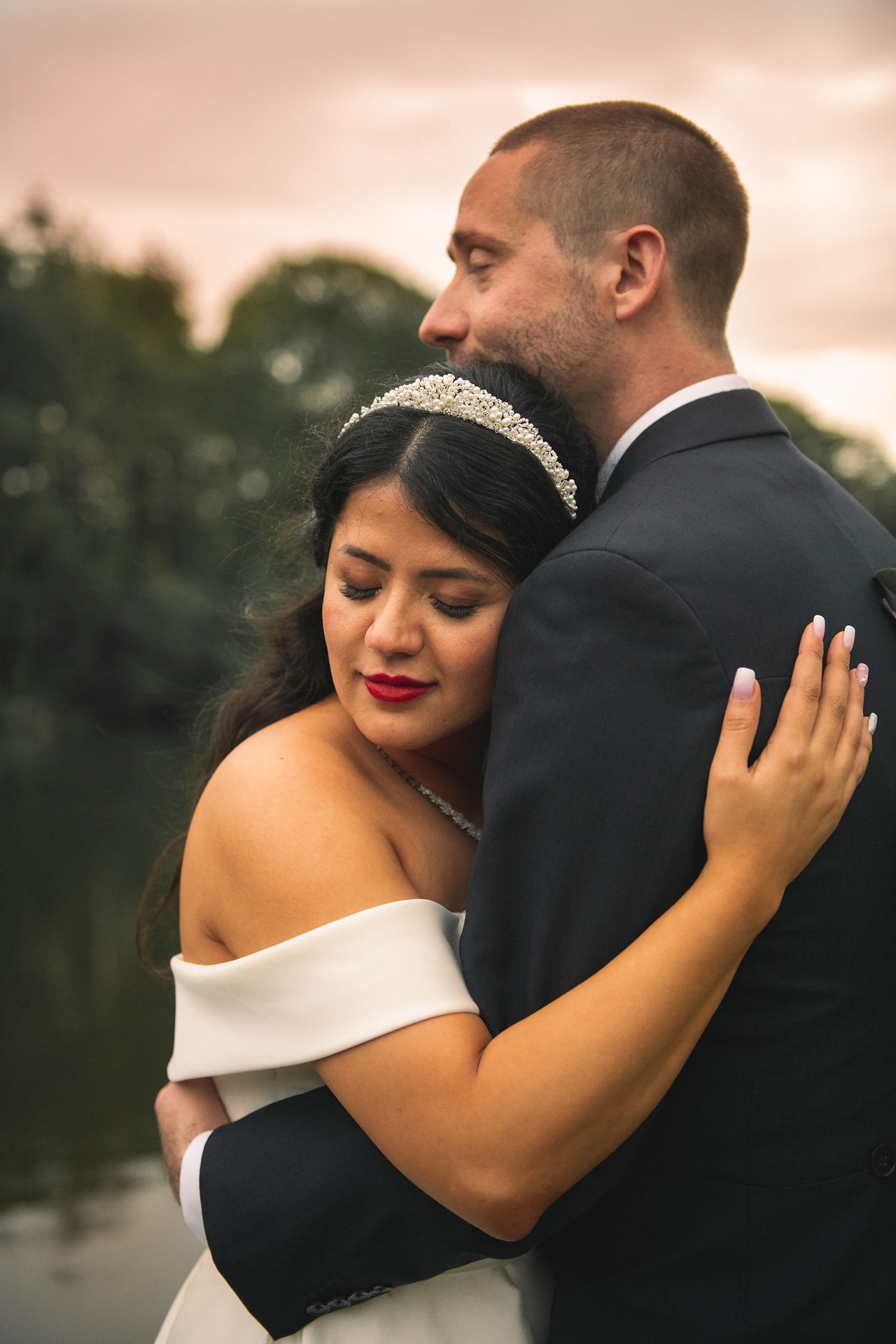 The bride and groom embrace with eyes closed during golden hour portraits at a wedding at Canada Lodge & Lake, Cardiff, by Swansea wedding photographer Katy Tainton Photography