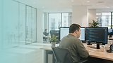 Person working at a desk in a modern office, using two computer monitors displaying software code and applications.