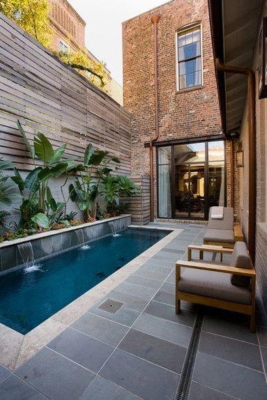 an outdoor swimming pool with lounge chairs and plants in the back yard